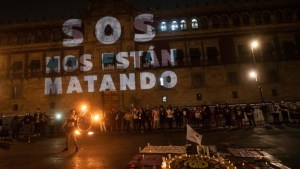 Las palabras "SOS nos están matando" se proyectan en Palacio Nacional mientras una mujer actúa con fuego durante una vigilia con familiares de víctimas de feminicidio y desapariciones forzadas en la Ciudad de México, el 28 de marzo de 2021. (Crédito: PEDRO PARDO/AFP vía Getty Images)