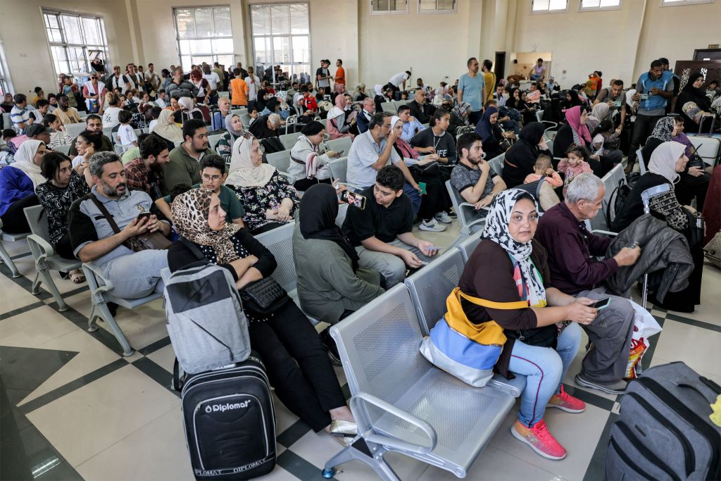 Varias personas sentadas en la zona de espera del paso fronterizo de Rafah, en el sur de Gaza, antes de cruzar a Egipto, el 1 de noviembre de 2023. (Crédito: MOHAMMED ABED/AFP vía Getty Images)
