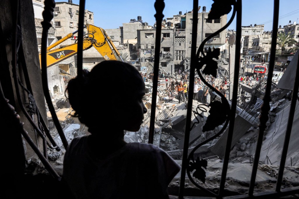 Se observa a una niña detrás de la malla metálica que cubría la ventana de un edificio que fue alcanzado por un bombardeo israelí en Rafah, en el sur de la Ciudad de Gaza, el 31 de octubre de 2023. (Foto de MOHAMMED ABED/AFP vía Getty Images)