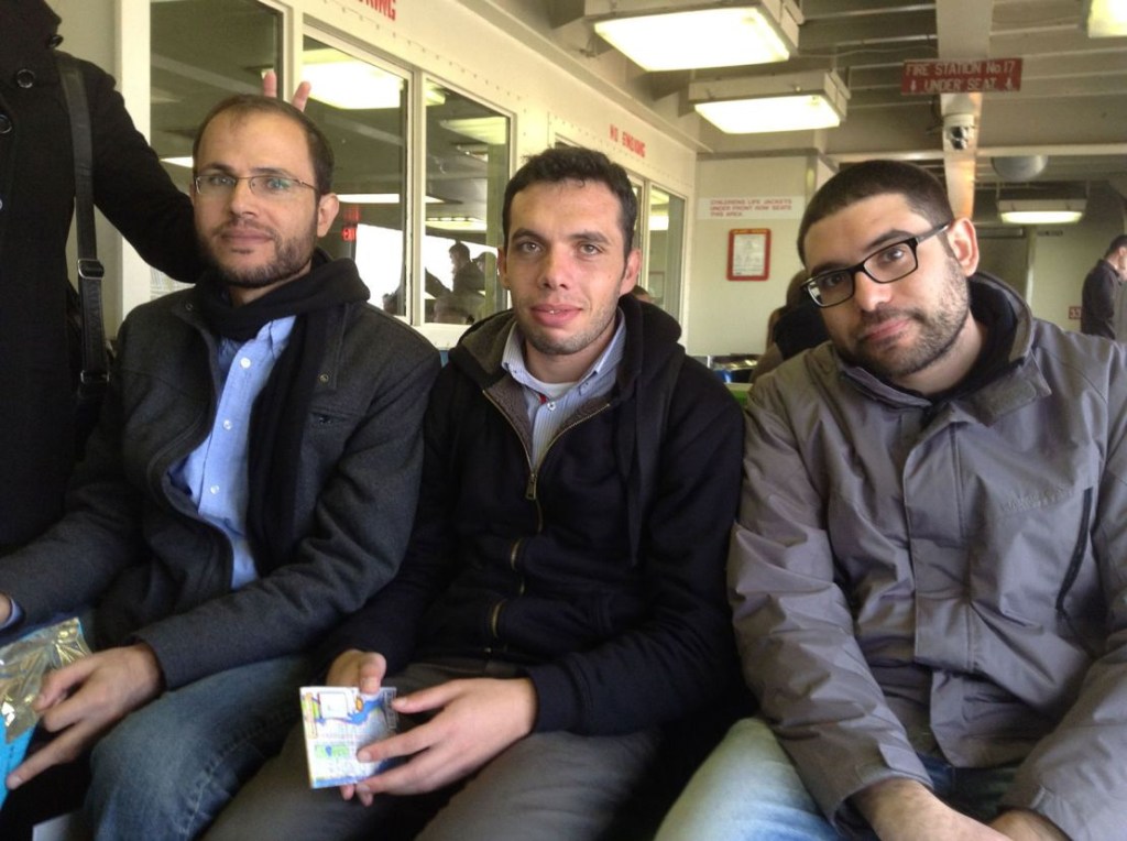 Refaat Alareer (izquierda) sentado con sus amigos y colegas, Yousef Aljamal (centro) y Jehad Abusalim (derecha), en el transbordador de Staten Island, en Nueva York, durante una gira literaria en 2014. (Foto cortesía de Jehad Abusalim)