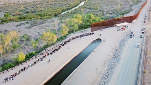 En una vista aérea, migrantes que buscan asilo en Estados Unidos esperan en fila cerca de la valla fronteriza para ser procesados por agentes de la Patrulla Fronteriza de Estados Unidos después de cruzar a Arizona desde México el 11 de mayo de 2023 en Yuma, Arizona. (Crédito: Mario Tama/Getty Images)