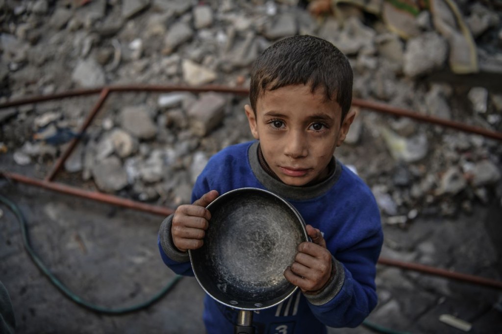 Un niño palestino sostenie una olla vacía mientras espera recibir alimentos distribuidos por voluntarios para familias palestinas desplazadas al sur de Gaza debido a los ataques israelíes, en Rafah, Gaza, el 22 de diciembre de 2023. (Abed Zagout/Anadolu via Getty Images)