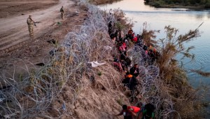 Los guardias nacionales de Texas observan cómo los migrantes se abren paso a través de alambre de púas después de cruzar el Río Bravo hacia Estados Unidos el 17 de diciembre de 2023 en Eagle Pass, Texas. (Crédito: John Moore/Getty Images)