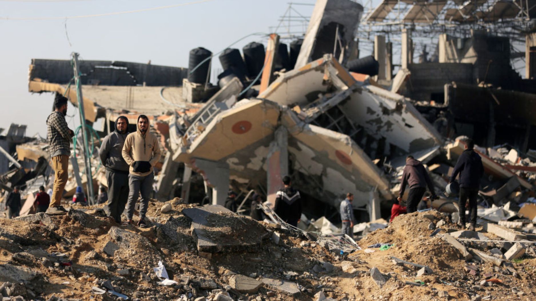 Un grupo de personas frente a un edificio derrumbado en el campo de refugiados de Al-Maghazi, en el centro de Gaza, el 16 de enero de 2024, en medio de los combates entre Israel y el grupo palestino Hamas. (Crédito: AFP vía Getty Images)