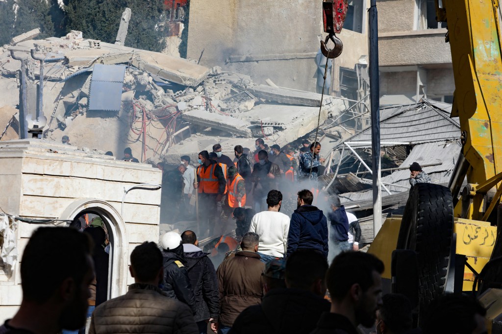 Personas y equipos de rescate se reúnen frente a un edificio destruido por un ataque israelí en Damasco el 20 de enero de 2024. (Crédito: Louai Beshara / AFP/Getty Images)