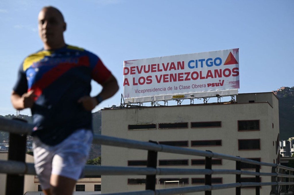 Un hombre pasa corriendo junto a un cartel del Partido Socialista Unido de Venezuela (PSUV), que dice "Devuelvan CITGO a los venezolanos", en Caracas el 27 de junio de 2023. (FEDERICO PARRA/AFP via Getty Images)