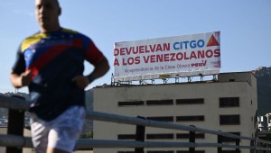 Un hombre pasa corriendo junto a un cartel del Partido Socialista Unido de Venezuela (PSUV), que dice "Devuelvan CITGO a los venezolanos", en Caracas el 27 de junio de 2023. (FEDERICO PARRA/AFP via Getty Images)