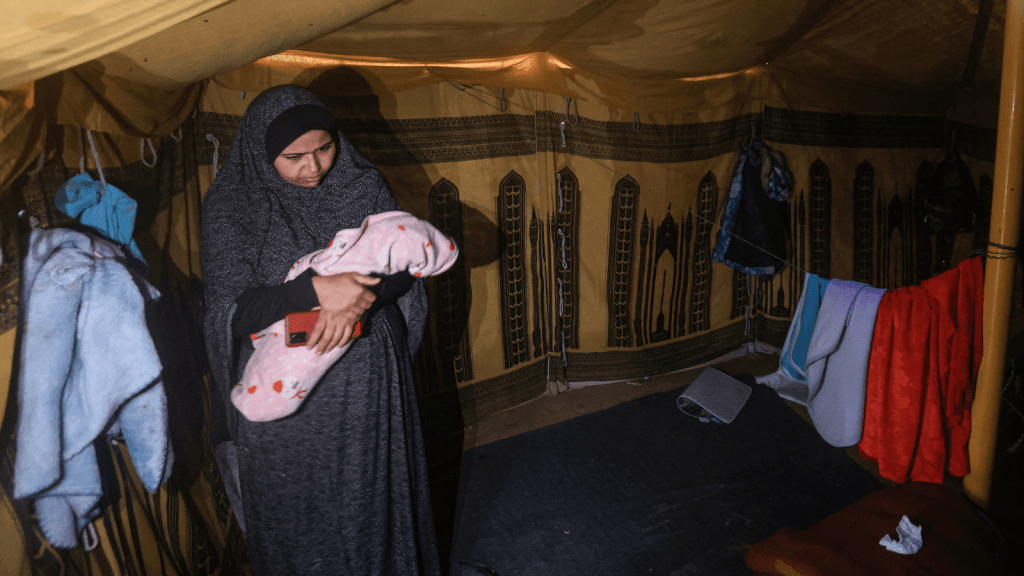Una mujer palestina sostiene a su bebé en su tienda de campaña en un campo para desplazados en Rafah, en el sur de Gaza, donde se han refugiado la mayoría de los civiles. (MAHMUD HAMS/AFP via Getty Images)