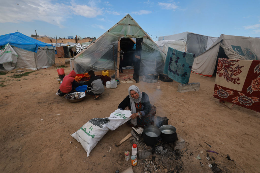 Una mujer palestina que huyó de Khan Younis prepara comida para su familia en un campamento establecido para personas desplazadas del norte en la región de Rafah, en el sur de la Franja de Gaza, el 15 de febrero de 2024. (Foto: Mohammed Abed/AFP via Getty Images).