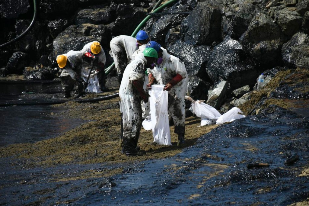 Workers clean up an oil spill on the beach at Rockley Bay in Scarborough, Trinidad and Tobago on February 10, 2024.  The origin of the vessel responsible for the spill is still unknown.  (Credit: Akash Bhutan/AP)