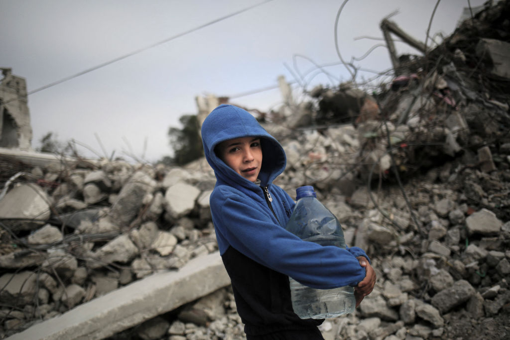 Un niño palestino lleva una botella de agua mientras pasa entre los escombros de las casas destruidas por los bombardeos israelíes en Rafah, en el sur de la Franja de Gaza, el 3 de marzo de 2024. (Foto: AFP vía Getty Images).