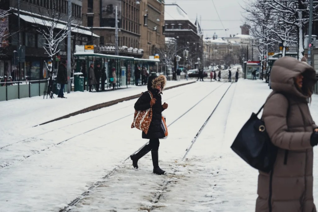 La gente cruza un ferrocarril cubierto de nieve en Helsinki, Finlandia, el 23 de abril de 2024, cuando un sistema climático inusual detuvo los tranvías de la ciudad. (Foto: Alessandro Rampazzo/Agencia Anadolu/Getty Images).