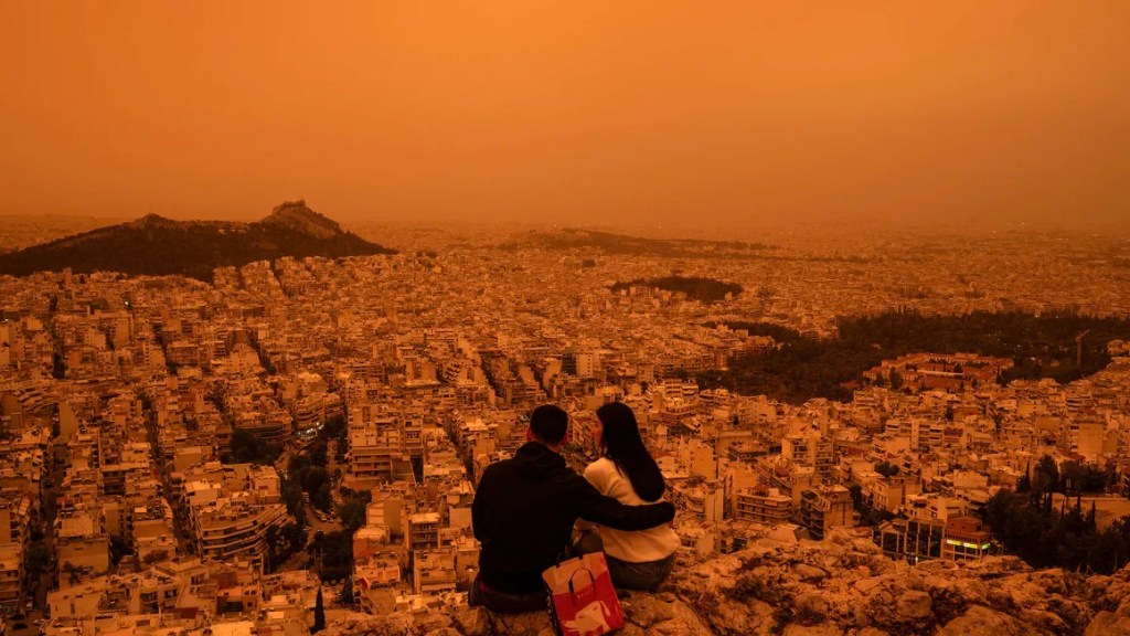 Una pareja sentada en la colina Tourkovounia en Atenas, mientras los vientos del sur transportan olas de polvo sahariano a Grecia, el 23 de abril de 2024. (Foto: Angelos Tzortzinis/AFP/Getty Images).