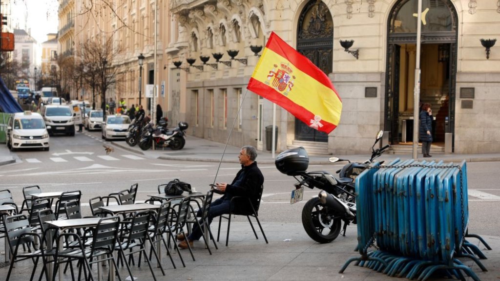 Un hombre con una bandera española sentado en una terraza mientras se lleva a cabo una sesión plenaria antes de la votación del controvertido proyecto de ley de amnistía del Gobierno, frente al Congreso de los Diputados en Madrid el 30 de enero de 2024. (Crédito: OSCAR DEL POZO/AFP vía Getty Images)