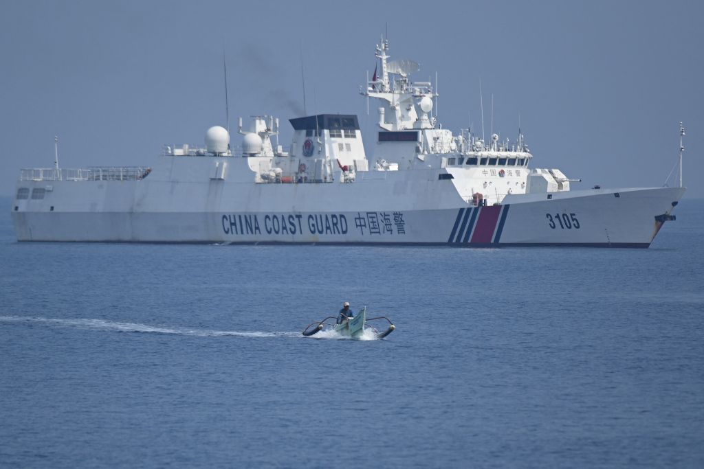 Un pescador filipino a bordo de su barco de madera navega junto a un barco de la Guardia Costera china cerca del dique de Scarborough, controlado por los chinos, en aguas en disputa del mar de China Meridional, en septiembre de 2023. (Foto: Ted ALJIBE/AFP) (Foto de TED ALJIBE/AFP vía Getty Images).