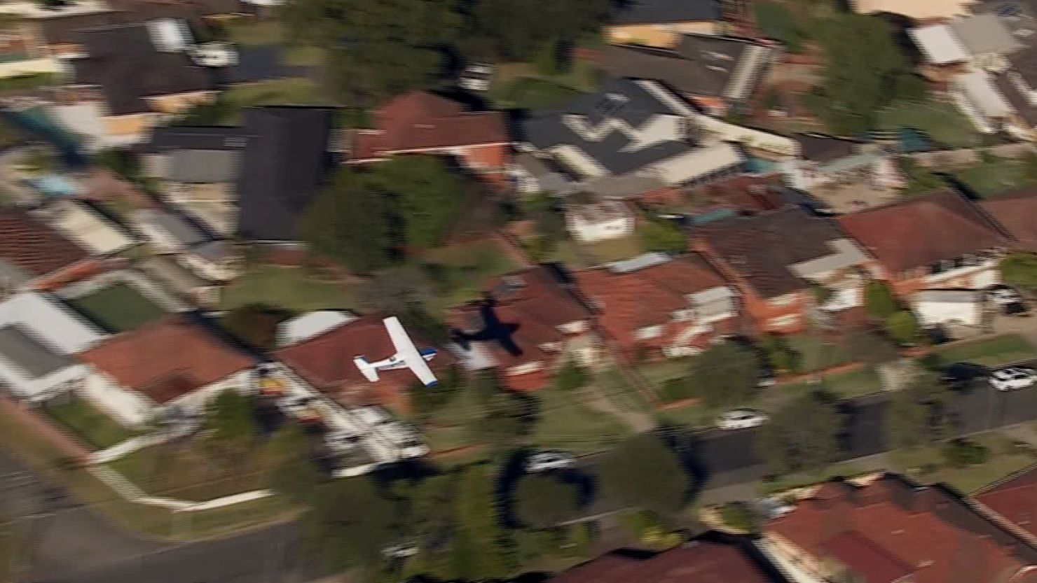 The plane loses power and scrapes the rooftops of the suburb before making a forced landing