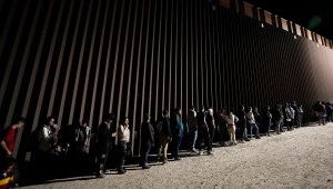 Migrantes se alinean contra un muro fronterizo cerca de Yuma, Arizona, en julio de 2023. (Foto: Gregory Bull/AP).