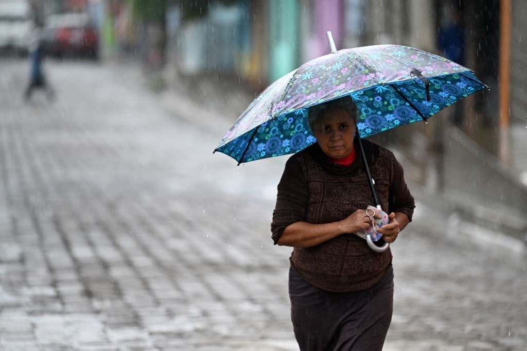 Una mujer se protege de la lluvia con un paraguas en Tacuba, El Salvador, el 17 de junio de 2024. (Foto de MARVIN RECINOS/AFP vía Getty Images)