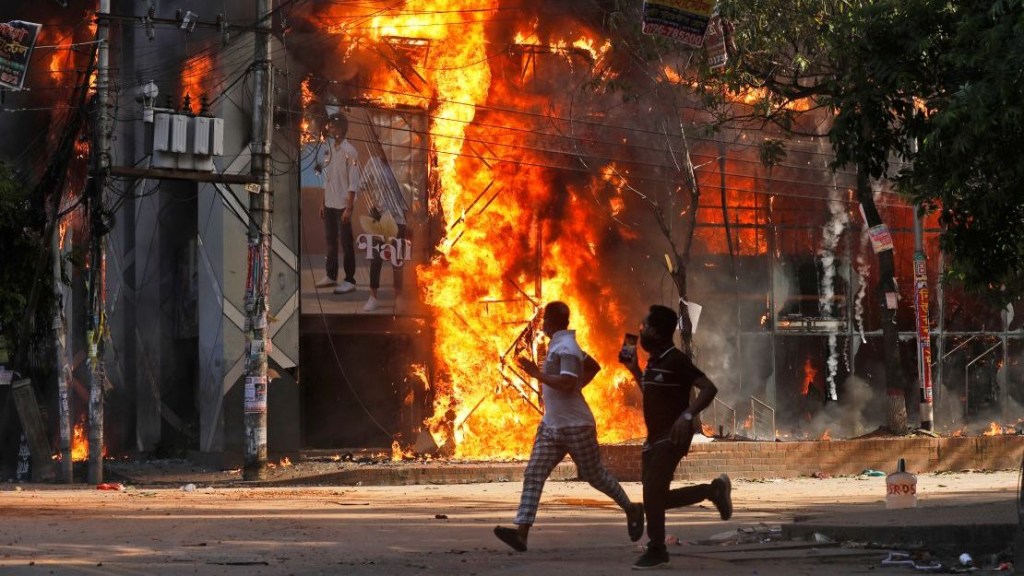 Varios hombres pasan corriendo junto a un centro comercial incendiado por manifestantes en Dhaka, Bangladesh, el 4 de agosto. (Crédito: Rajib Dhar/AP)