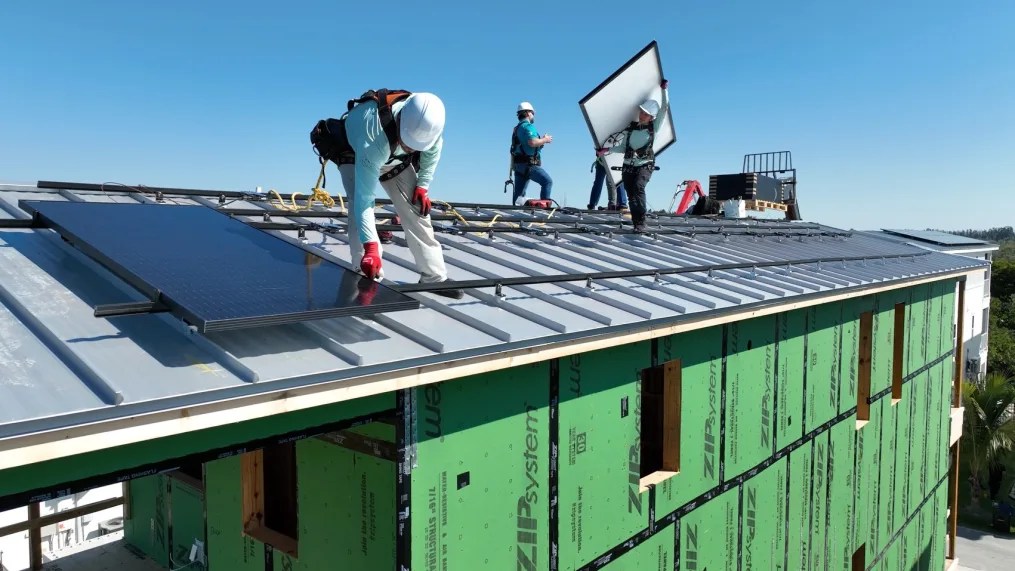 Trabajadores fijan paneles solares a las juntas verticales elevadas de los tejados para evitar que salgan volando durante violentas tormentas, en abril de 2024. (Julian Quinones/CNN/Archivo)