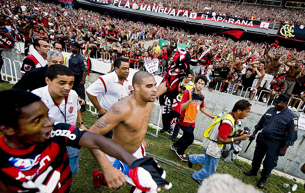 El jugador del Flamengo Adriano (al centro, sin playera) corre para celebrar con sus seguidores la victoria de su equipo en el campeonato brasileño tras ganar por 2-1 en su partido de la última fecha contra el Gremio, en el estadio Maracaná, el 6 de diciembre de 2009 en Río de Janeiro, Brasil. Así, sin playera, además de estar descalzo, es como a Adriano le gusta pasearse en Vila Cruzeiro. (ANTONIO SCORZA/AFP vía Getty Images)