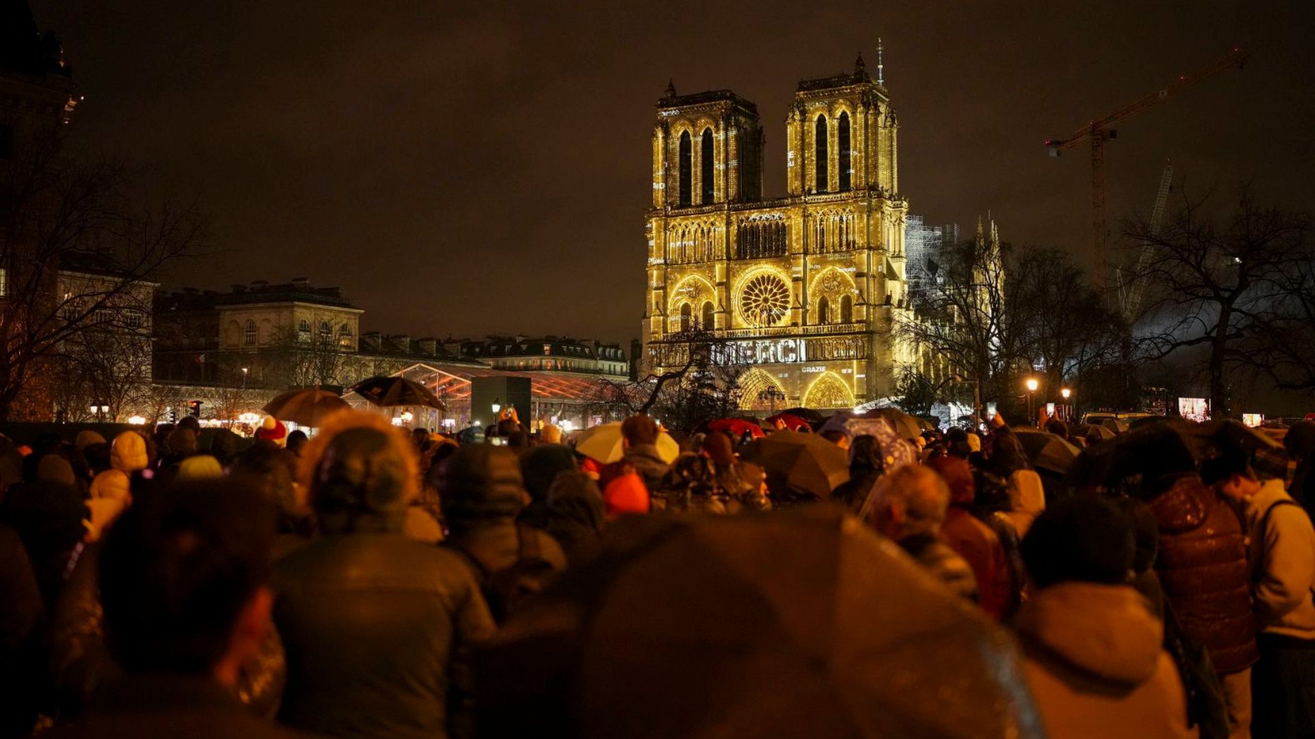 Espectadores se reúnen fuera de Notre Dame mientras se ilumina con las palabras "Gracias" en múltiples idiomas. (Crédito: Alessandra Tarantino/AP)