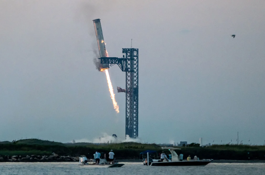 Enormes pinzas de metal agarran el cohete propulsor Super Heavy de Starship mientras regresa a la plataforma de lanzamiento en Starbase cerca de Brownsville, Texas, después del vuelo de prueba del 13 de octubre. La maniobra fue una novedad en el intento de SpaceX de hacer reutilizable el cohete. (Foto: Sergio Flores/AFP/Getty Images)