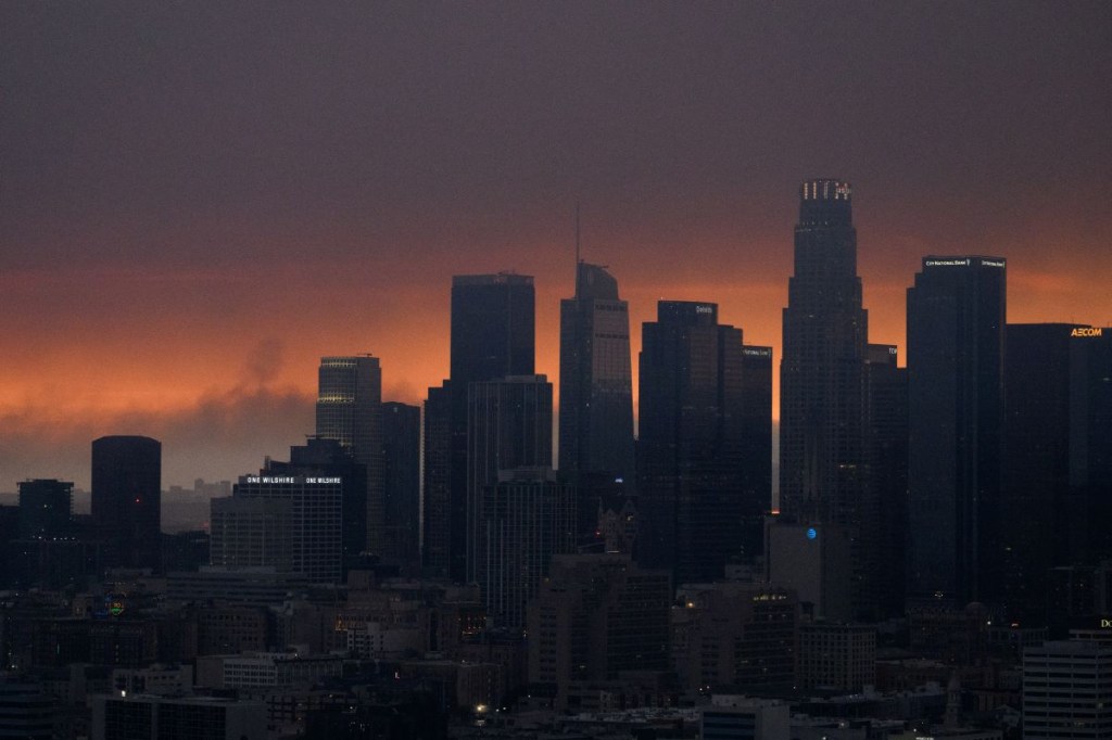 Una imagen aérea muestra el humo del incendio Palisades elevándose detrás del horizonte del centro de Los Ángeles mientras la ciudad está cubierta por una neblina debido a los incendios forestales que arrasan Los Ángeles, California, el 8 de enero de 2025. (Foto de PATRICK T. FALLON/AFP vía Getty Images)